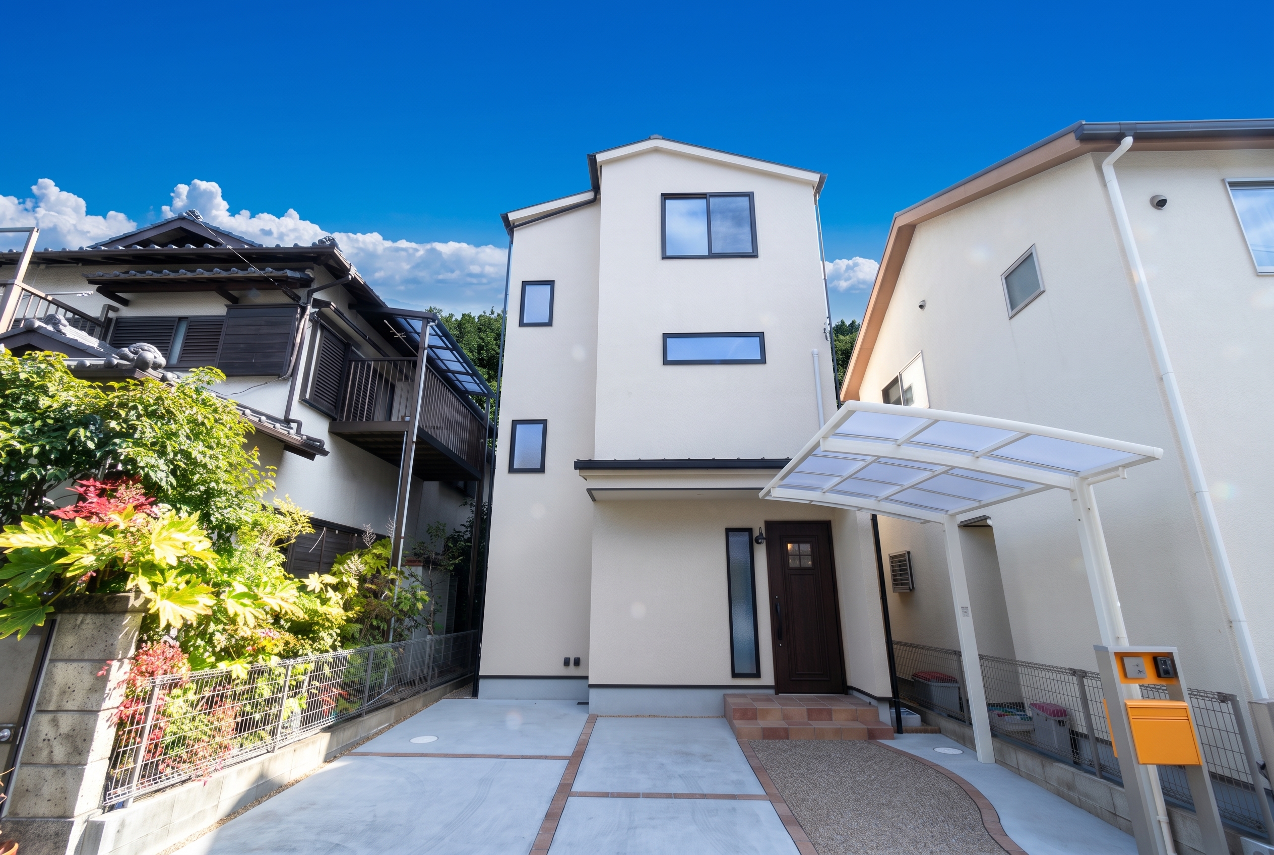 青空の下に建つ、白い外壁のシンプルな3階建て住宅の外観。広々とした駐車スペースや白いサイクルポート、木目調の玄関ドアへ続くアプローチを備えています。