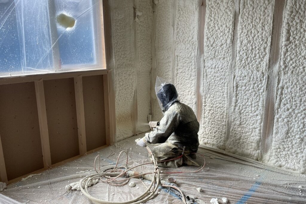 住宅の壁面に断熱材の吹付ウレタンフォームを施工している、防護服を着用した作業員