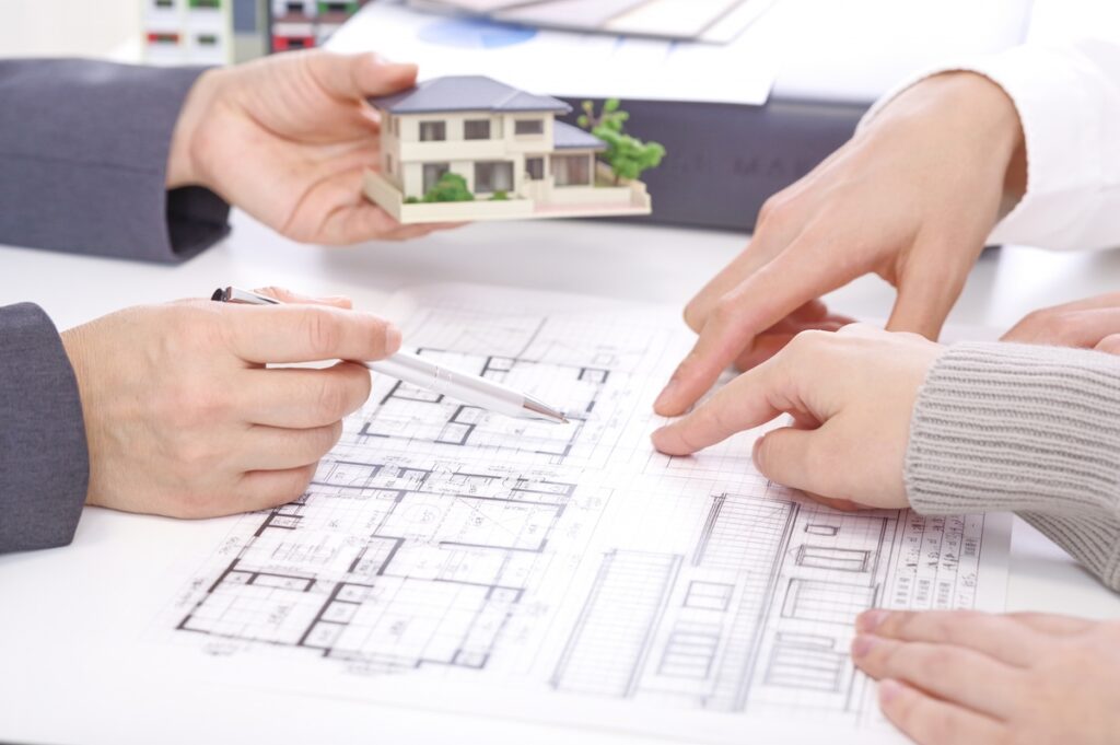建築図面を指差しながら、家の模型を囲んで打ち合わせを行う工務店スタッフと施主の手元