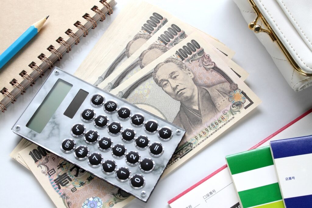家づくりに必要な自己資金や予算管理をイメージさせる、一万円札の束と大理石調の電卓、そして複数の銀行通帳。