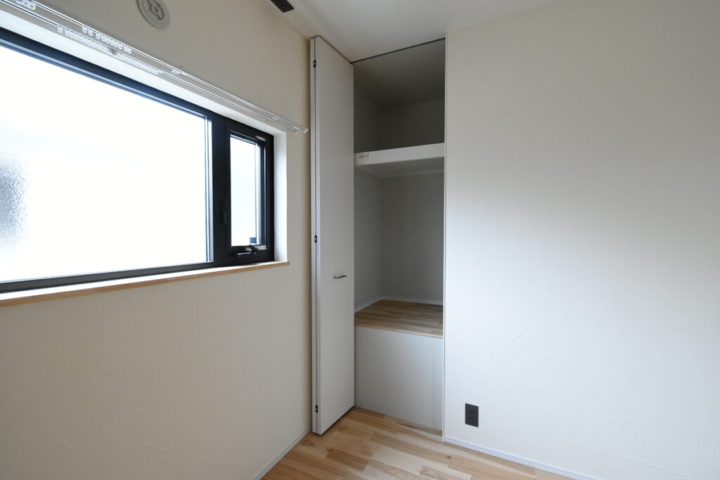 表情豊かな塗り壁と無垢材の床が調和した室内。黒いサッシの窓と、中段に棚を設けたシンプルなクローゼットが機能的に配置されている。