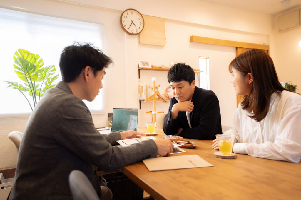 木の質感を生かした温かみのある打ち合わせスペースで、資料を見ながらスタッフの説明を真剣に聞く家づくり相談中の夫婦。