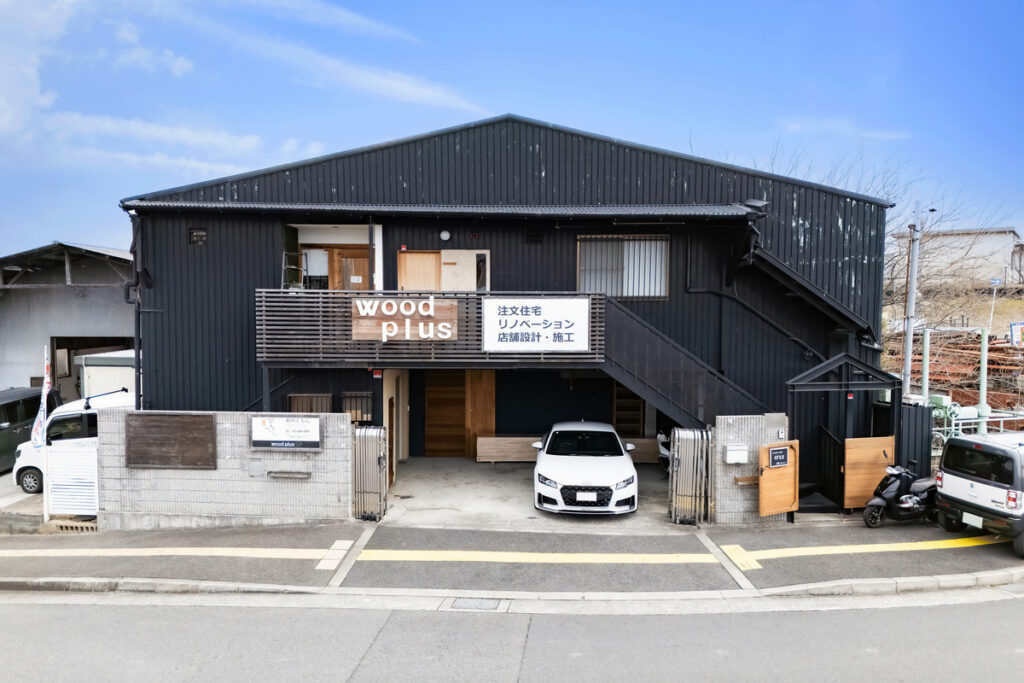 黒いガルバリウムの外装に「woodplus」の看板が掲げられた、注文住宅やリノベーションを手掛ける工務店のオフィス外観