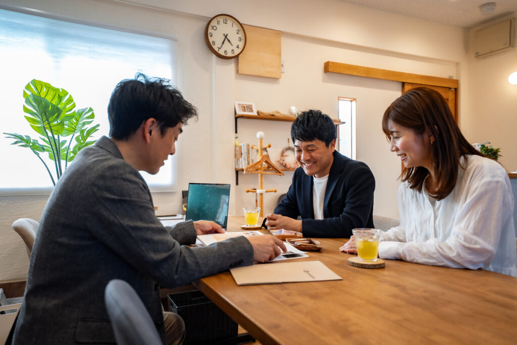 木のぬくもりあふれる空間で、資料を見ながら家づくりの相談を丁寧に進めるスタッフと施主夫婦。