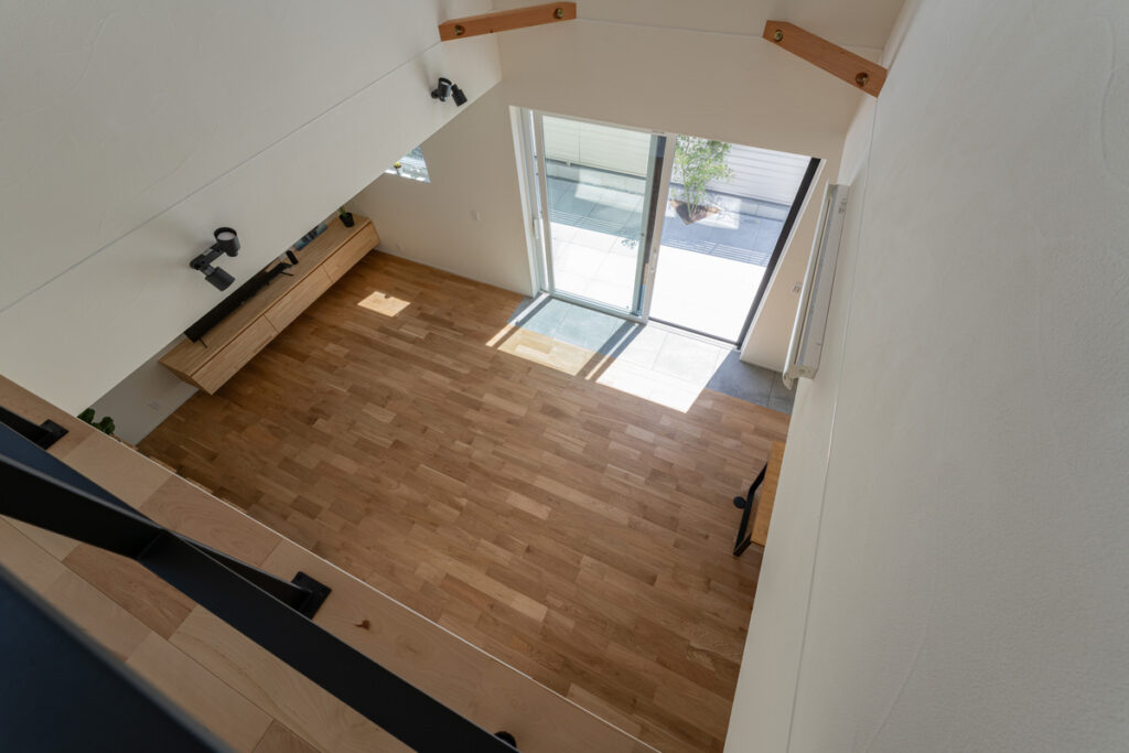 2階のキャットウォークや階段側から見下ろした、大きな掃き出し窓から光が差し込む吹き抜けのリビング