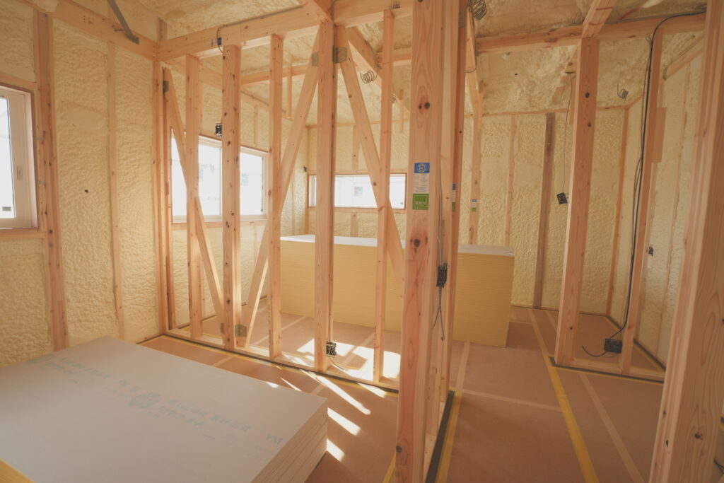 柱や梁の構造が見え、壁や天井にしっかりと断熱材が吹き付けられている施工中の住宅内部の様子