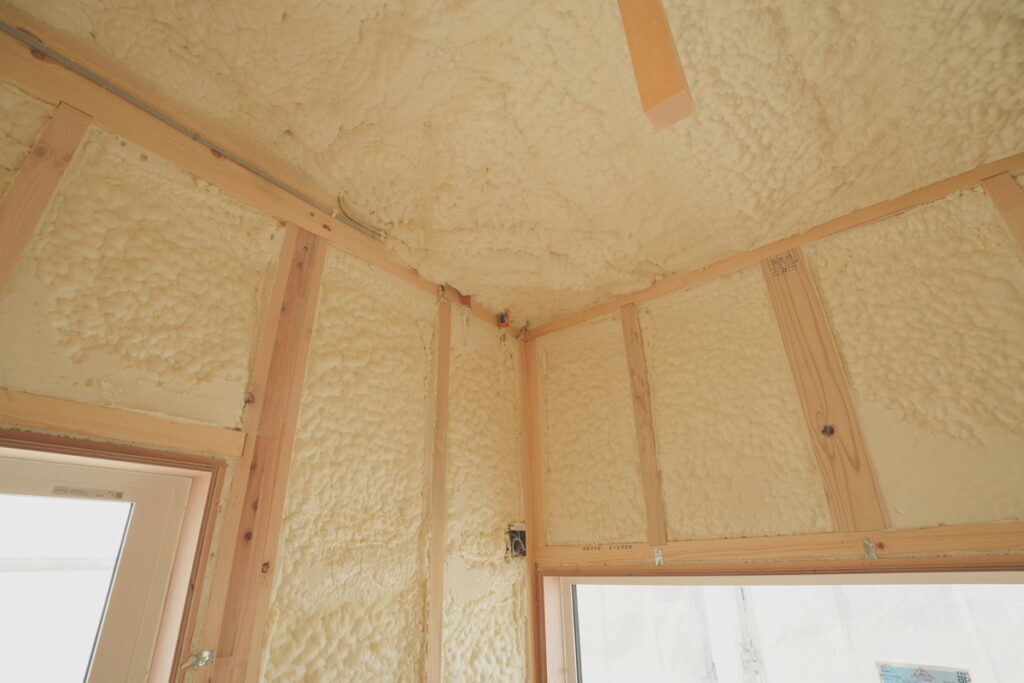 住宅の建築施工現場において、壁や天井の木枠の間に発泡ウレタン断熱材が隙間なく吹き付けられている様子