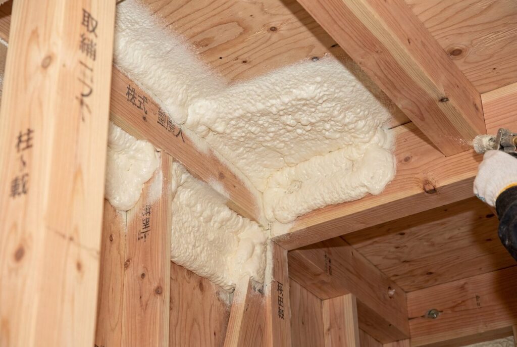 木造住宅の建築現場で、柱や梁の接合部や隙間にスプレーガンを使って吹付けウレタン断熱材を施工している様子