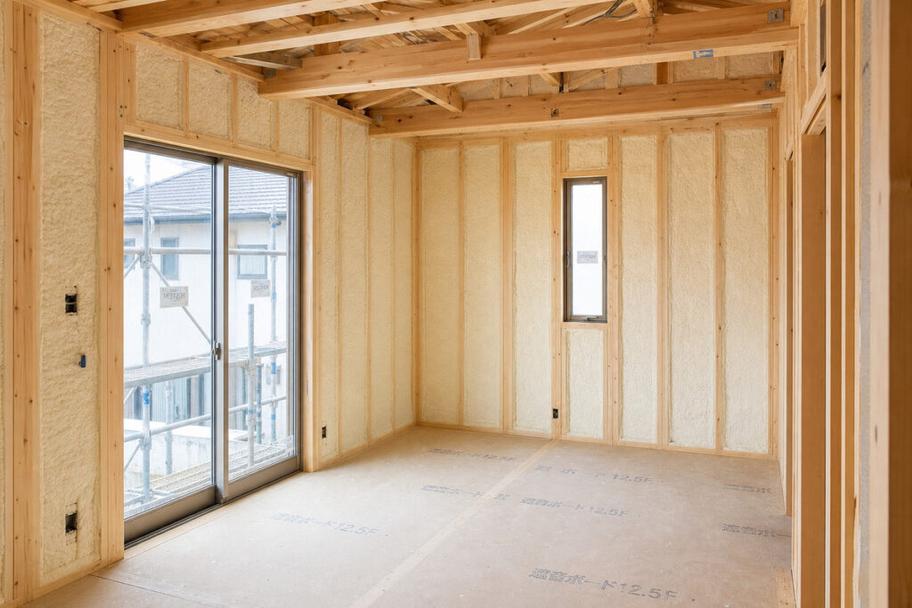 ④建築中の木造住宅の壁内に白い吹き付け断熱材が施工されている工事現場