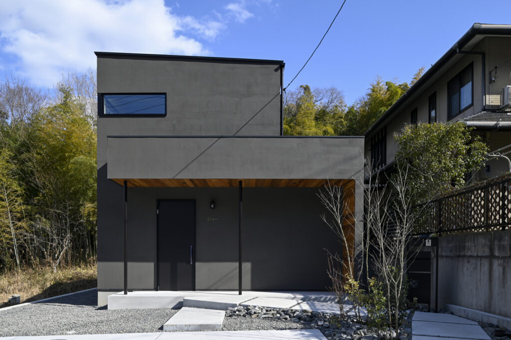 ダークグレーの外壁とキューブ型のモダンなフォルムが特徴的な新築住宅の外観。玄関ポーチの木目調の軒天がデザインのアクセントになっています。