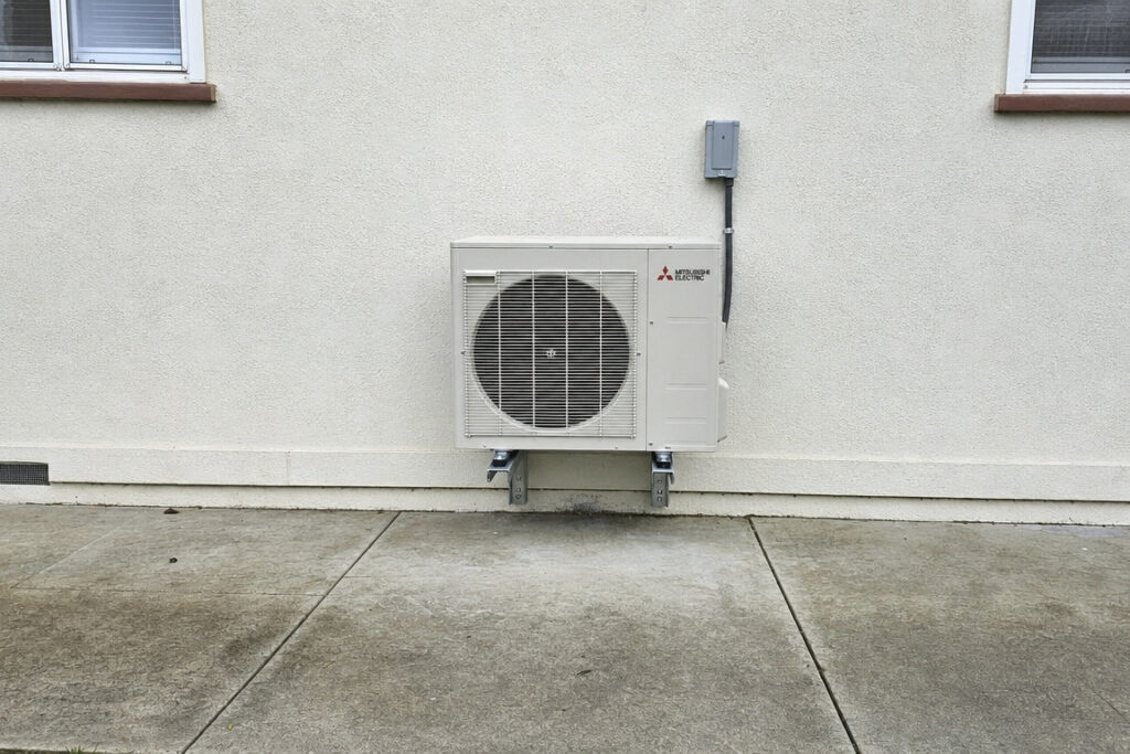 白い外壁に沿ってコンクリート土間に設置された、三菱電機製のエアコン室外機。配管もすっきりとまとめられています。