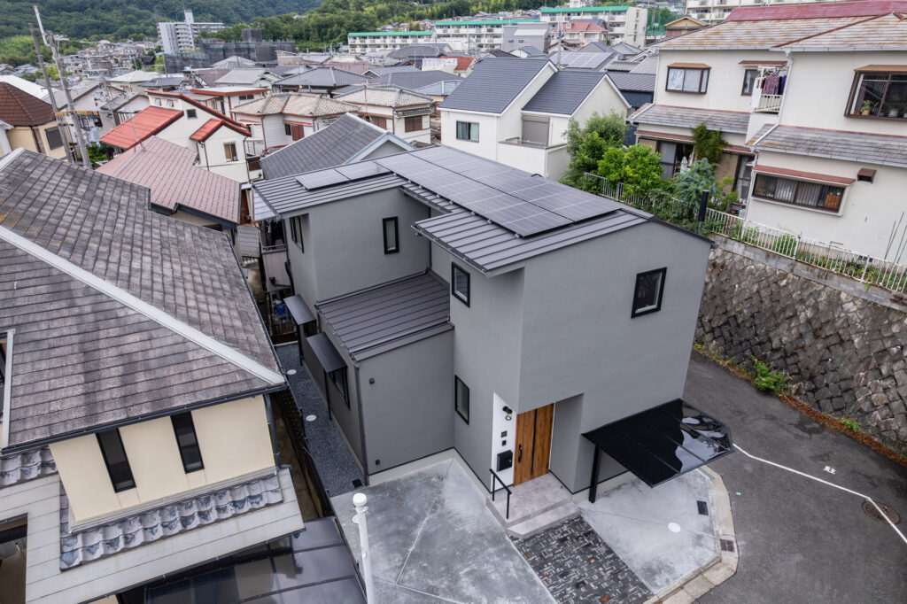 屋根に太陽光パネルを搭載した金属屋根とグレーの外壁が特徴的な、モダンデザインの住宅外観。