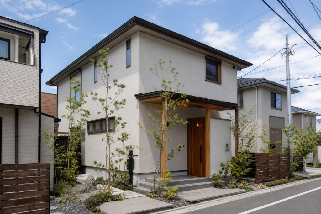 白い塗り壁調の外壁に木製の柱と深い軒のポーチが調和する、和モダンな2階建て住宅の外観。豊かな植栽と飛び石のアプローチが配置されています。