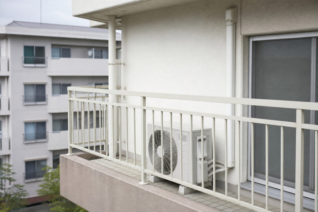 マンションのタイル張りバルコニーに設置されたエアコンの室外機。配管はスリムダクトを用いて外壁に沿って美しく施工されている。