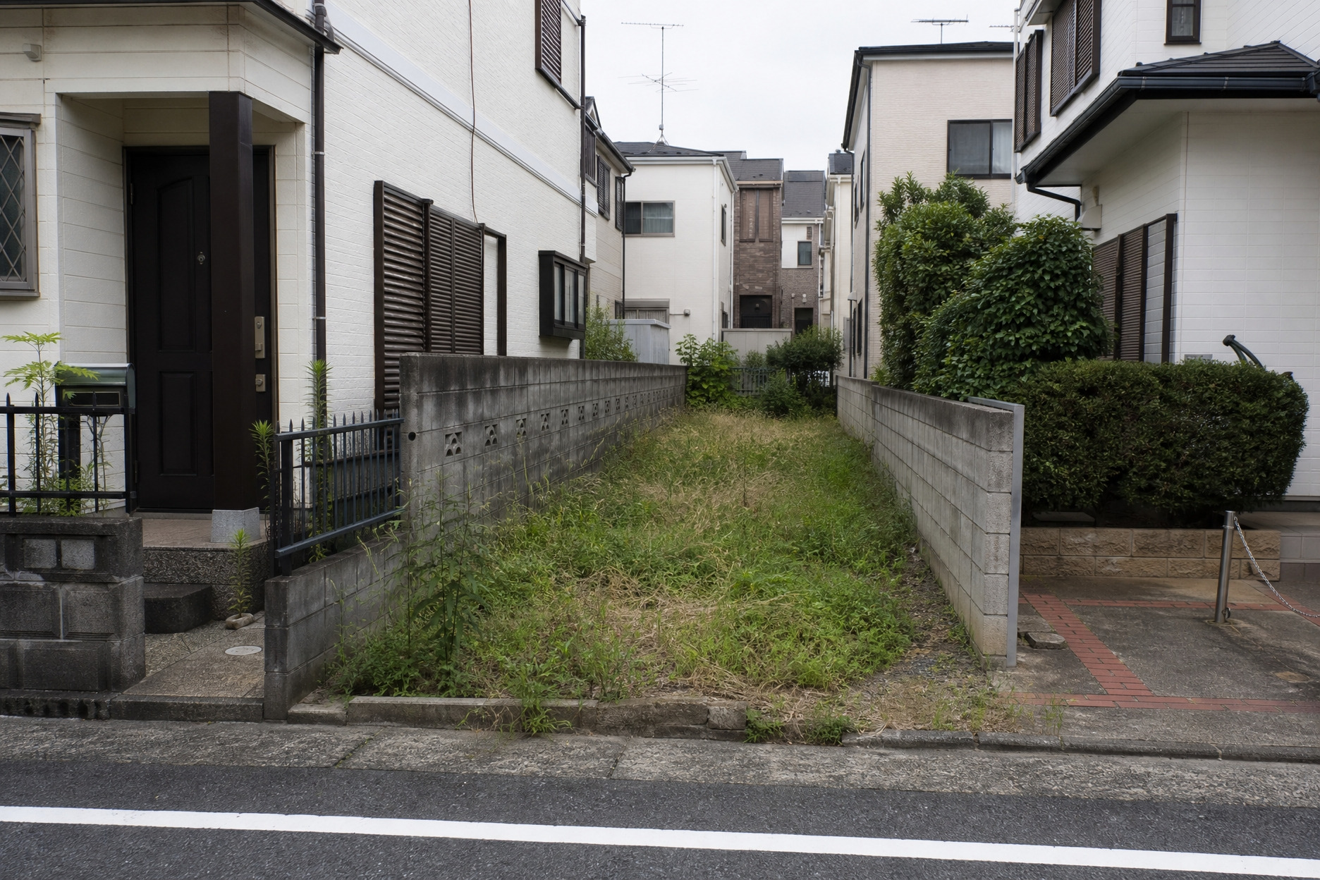 住宅街にある、両サイドをブロック塀に囲まれた細長い形状の空き地。雑草が生い茂る土地ですが、視野を広げることで狭小地や変形地での家づくりの選択肢となります。