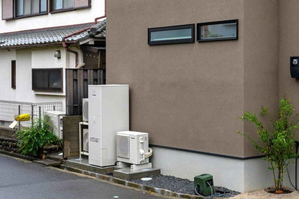 ブラウン系の外壁の住宅の屋外に設置された、エコキュートの貯湯タンクユニットとヒートポンプユニット。