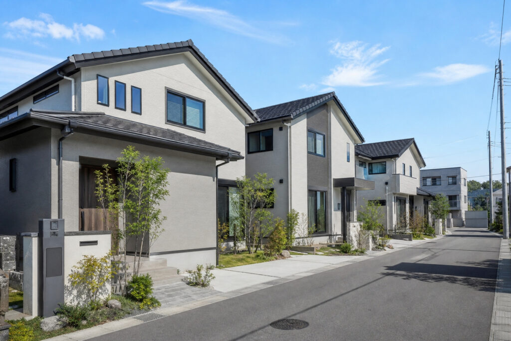 明るいグレーの外壁に黒の屋根とサッシがアクセントになった、シンプルモダンな住宅が並ぶ分譲地の外観。豊かな植栽が玄関アプローチを引き立てています。