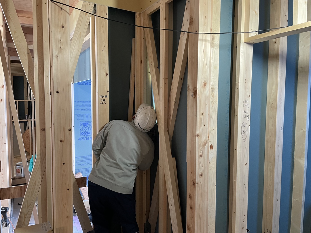 木造住宅の建築現場で、職人が柱や筋交いが組まれた壁面の構造部分を確認している様子。