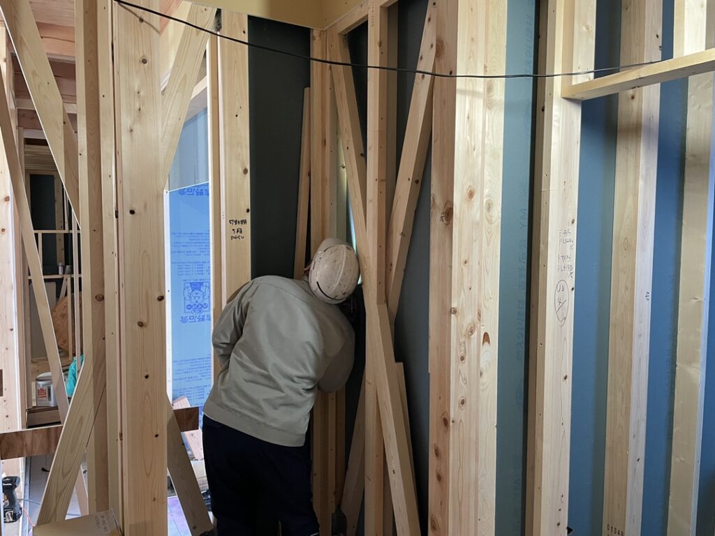 木造住宅の建築現場で、職人が柱や筋交いが組まれた壁面の構造部分を確認している様子。