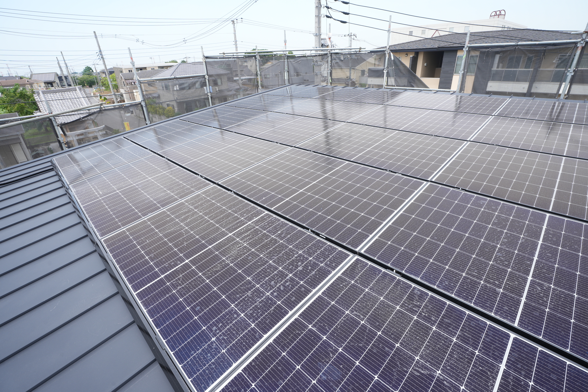 施工中の足場に囲まれた、緩やかな勾配の金属屋根に隙間なく敷き詰められた多数の太陽光パネル。