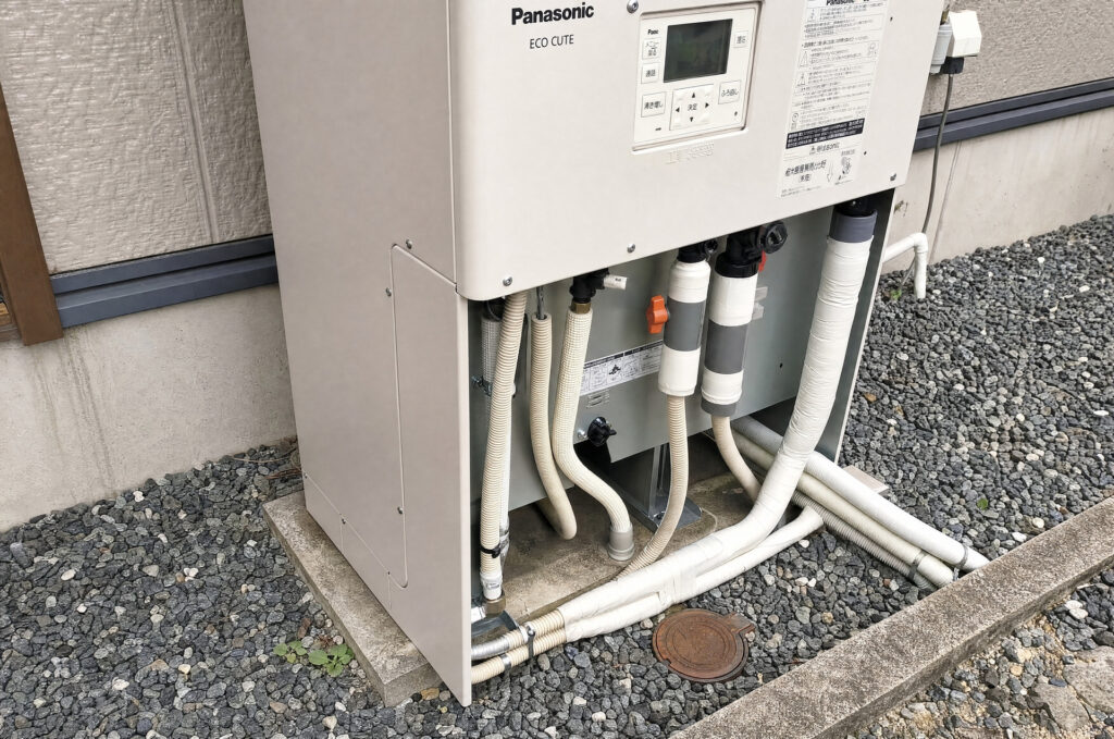 下部のカバーが外され、断熱材が巻かれた配管やバルブ類が露出しているパナソニック製エコキュートの点検時の様子。