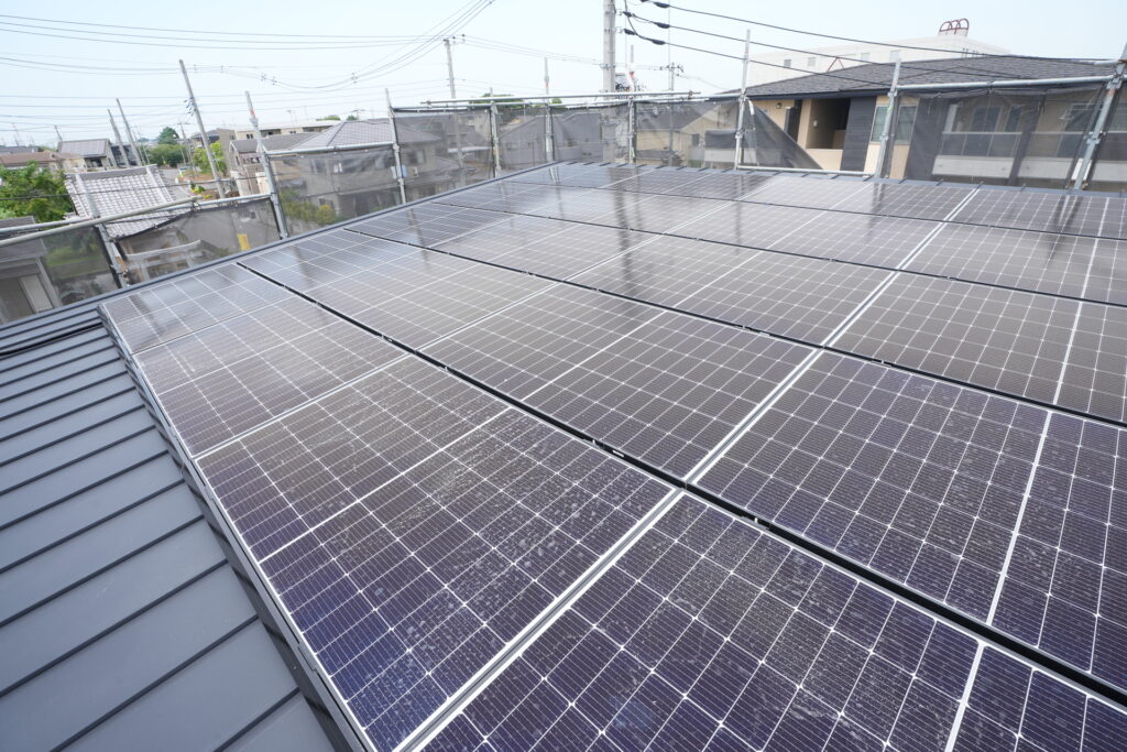 施工中の足場に囲まれた、緩やかな勾配の金属屋根に隙間なく敷き詰められた多数の太陽光パネル。