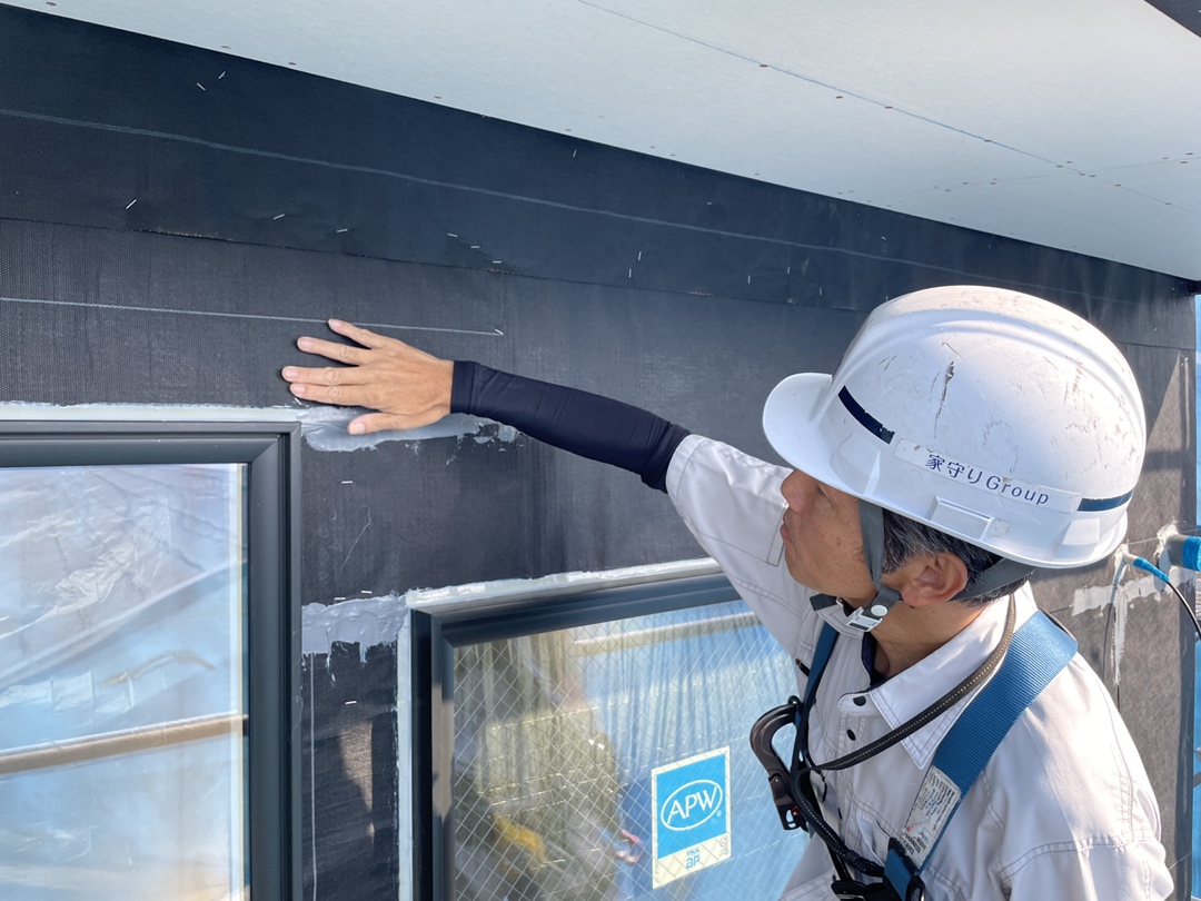 ヘルメットを着用した施工スタッフが、サッシ周りの防水シートや気密処理の施工箇所を丁寧に手で確認している様子