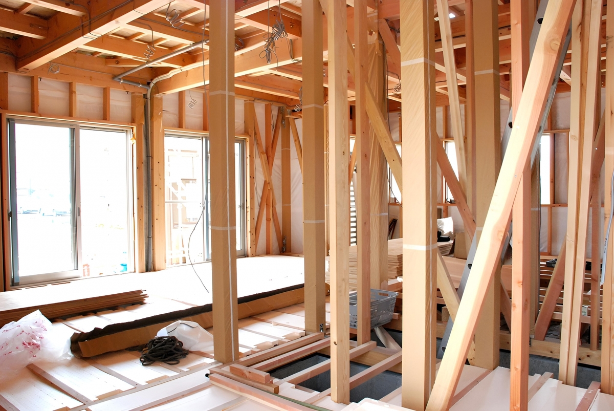 建築中の木造住宅の内部。無垢材の柱や梁、筋交いなどの構造体や、窓サッシが取り付けられた様子が確認できます。