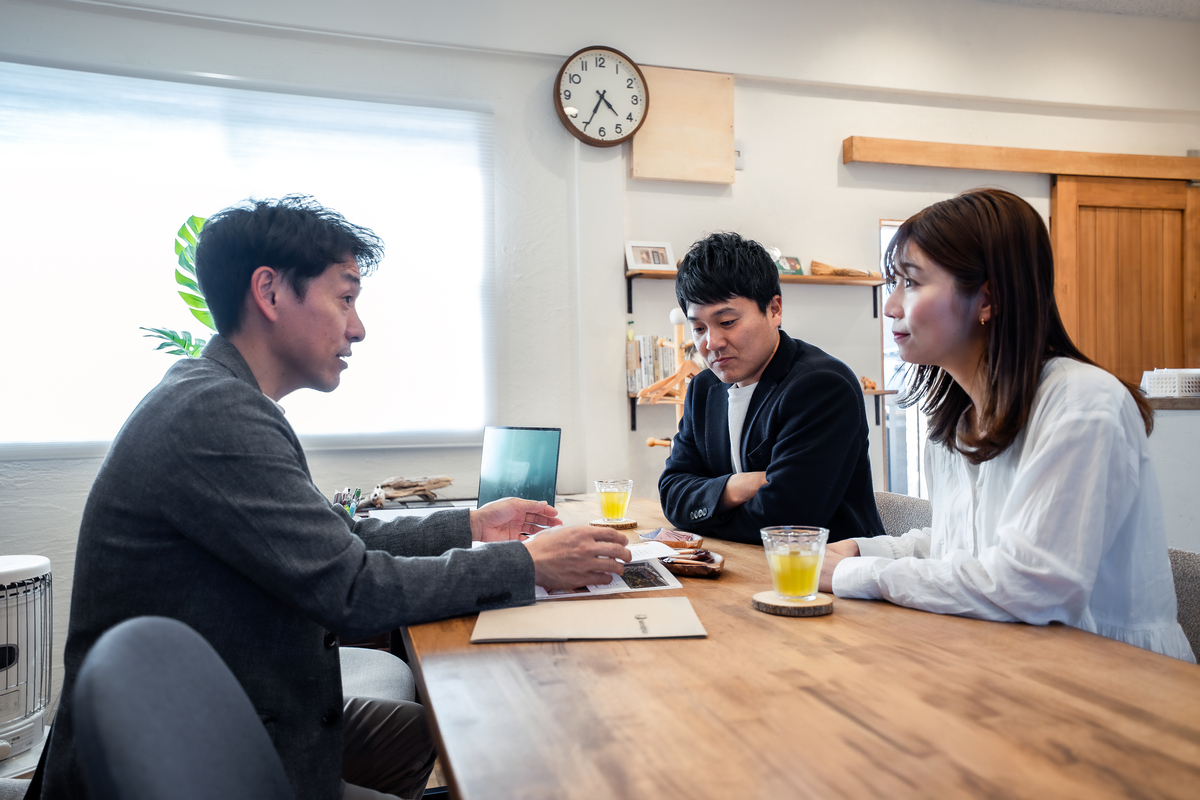 打ち合わせテーブルで資料を広げる工務店スタッフの説明を、真剣な表情で聞き入る家づくり検討中の夫婦