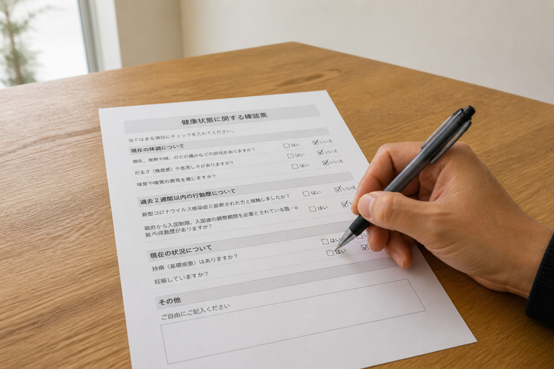 ナチュラルな質感の木製デスクの上で、「健康状態に関する確認票」にボールペンで記入しています。