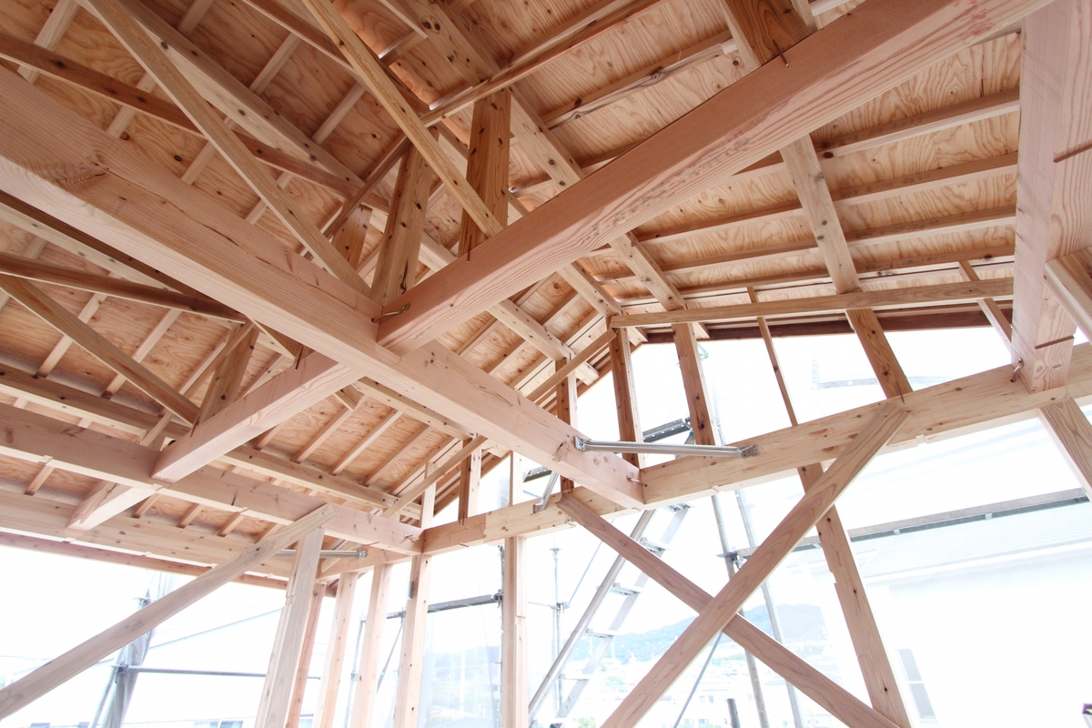 住宅の骨組みとなる梁や柱、筋交いがしっかりと組まれ、屋根下地の構造用合板が施工された明るい建築中の木造躯体内観。