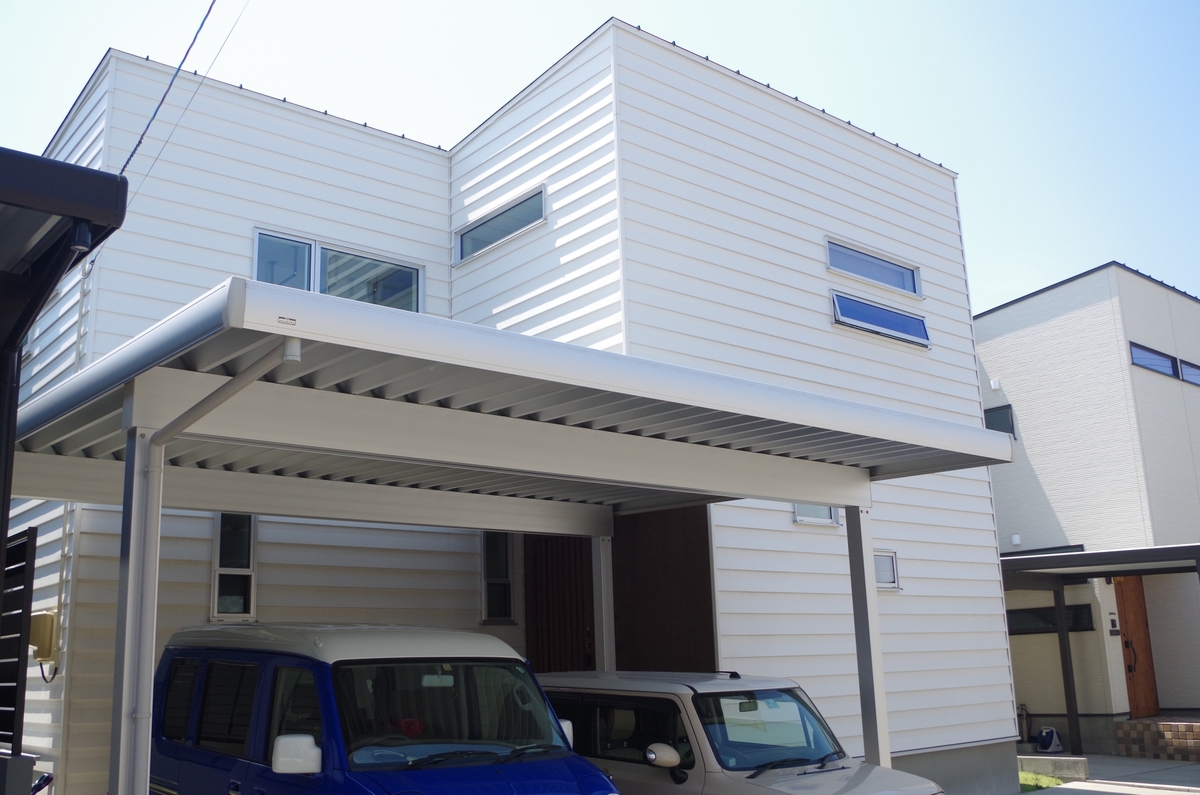 白い横張りの外壁が特徴的なモダンなデザインの住宅外観と、手前に設置された大型の金属製カーポート。