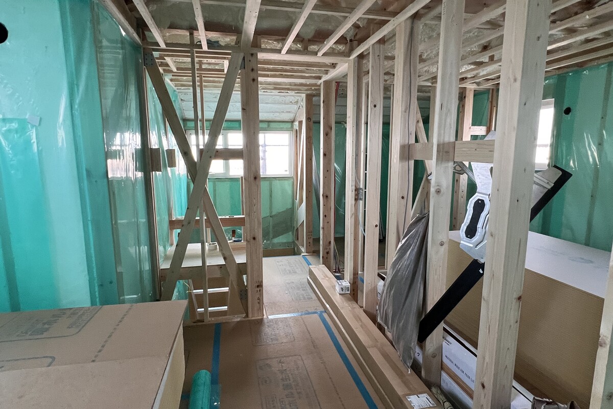 建築中の木造住宅の内部。壁や天井に吹き付け断熱材が施工され、その上から緑色の気密シートが丁寧に張られた、高気密・高断熱の家づくりを支える施工風景。