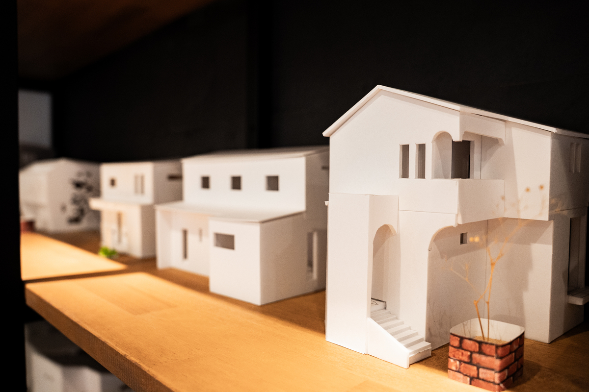 木製カウンターの上に並ぶ、アール壁やバルコニーの形状を忠実に再現した白い住宅建築模型