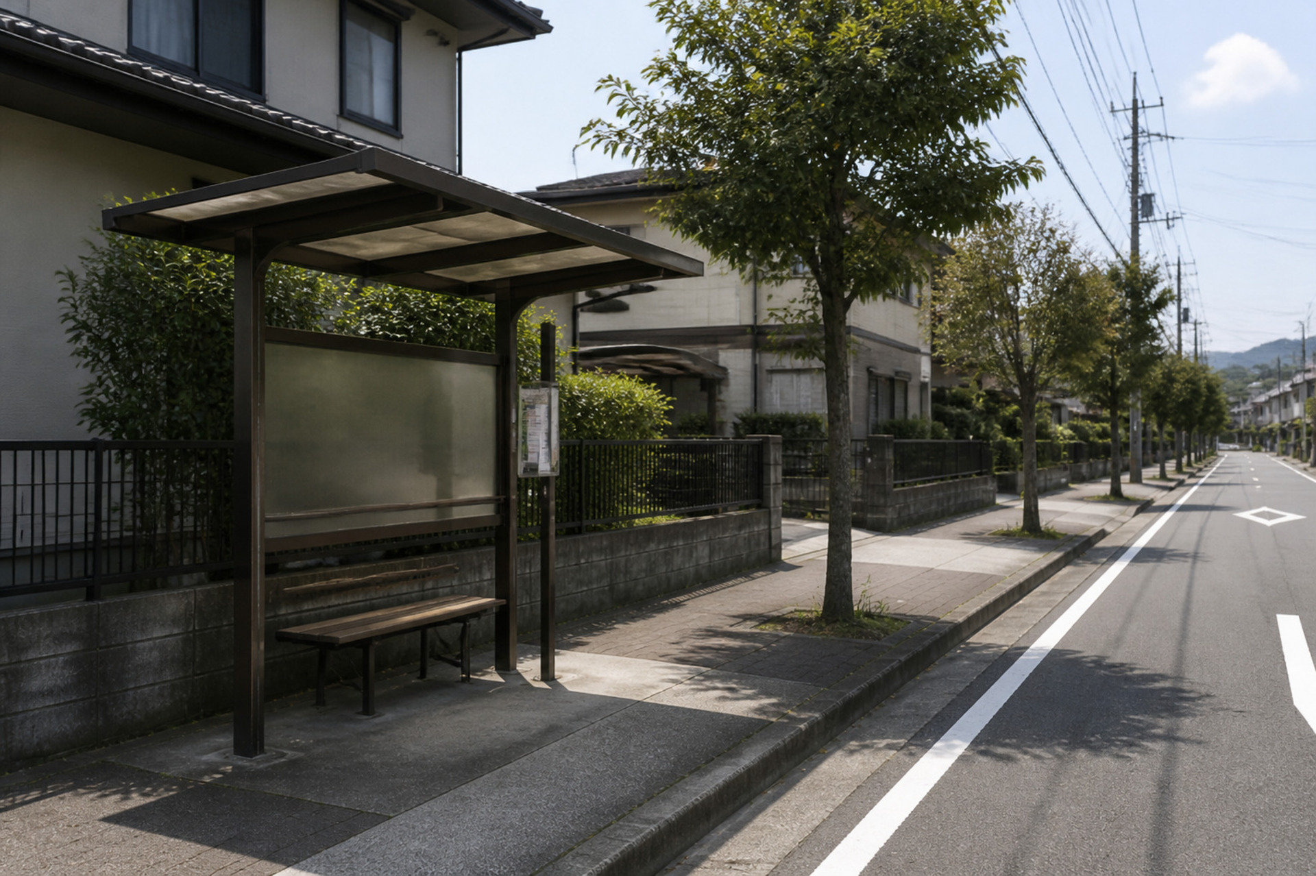閑静な住宅街の通り沿いに整備された、木陰のある清潔感のあるバス停と歩道の風景。