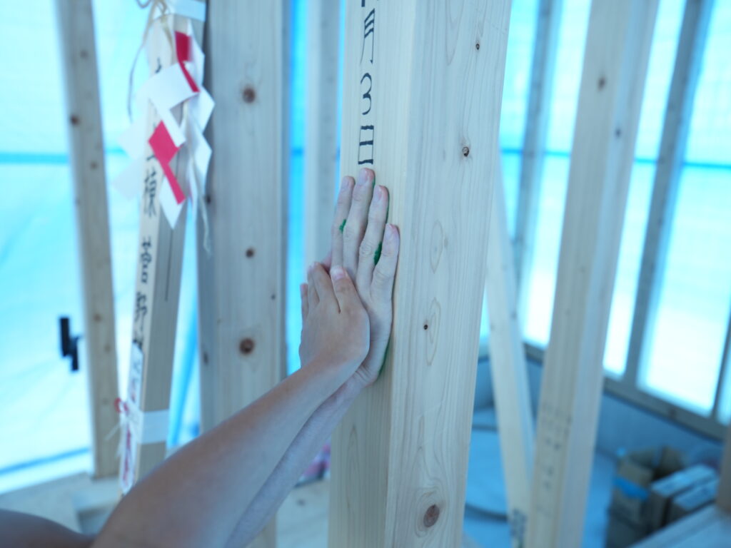 家づくりの記念となる手形式。真新しい構造柱にご家族が手を重ねて緑色の手形を押しており、奥には上棟を祝う御幣が飾られています。
