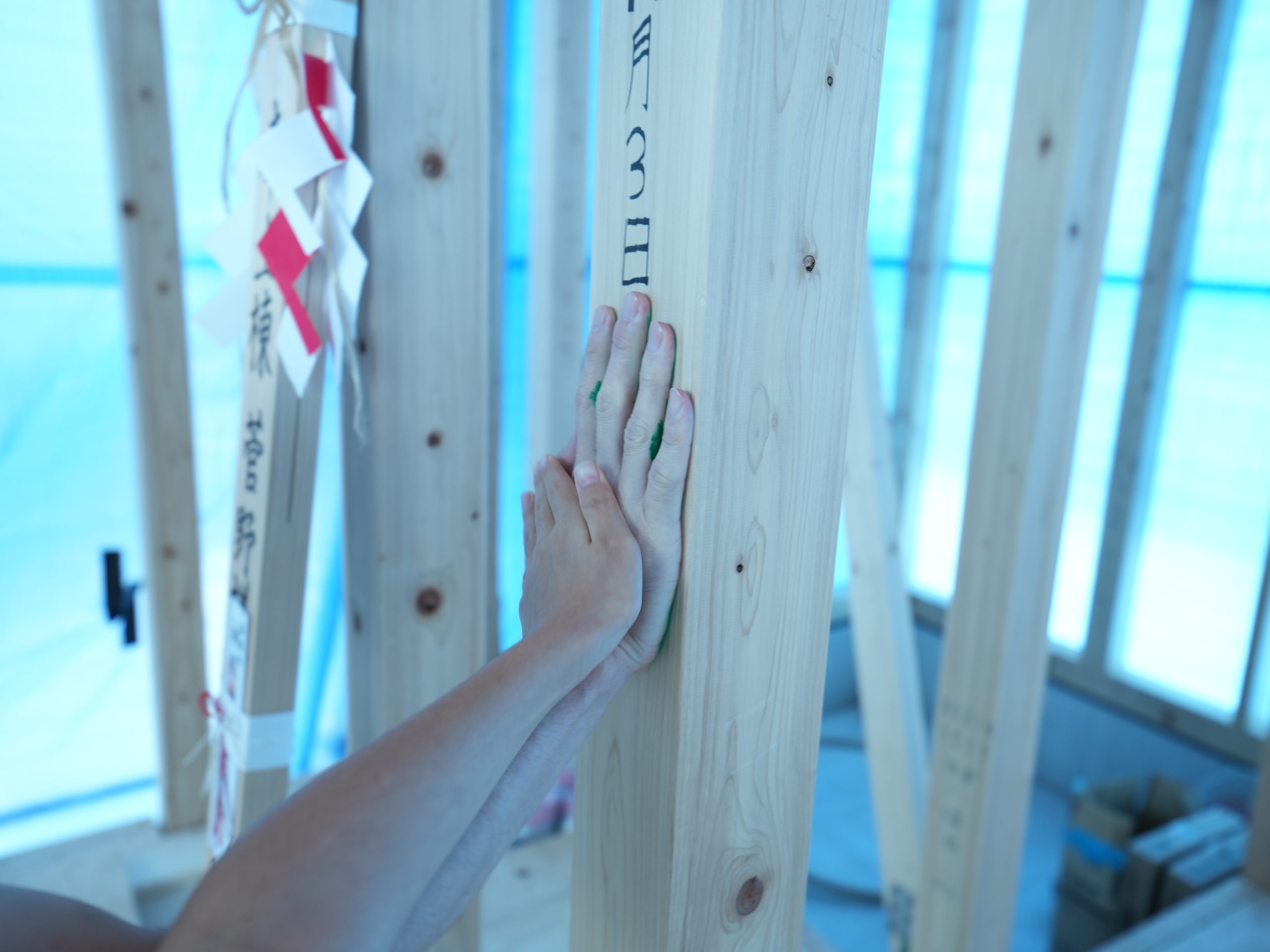 上棟の記念となる手形式。御幣が飾られた建築現場にて、真新しい無垢の構造柱にご家族が手を重ねて緑色の手形を押しています。
