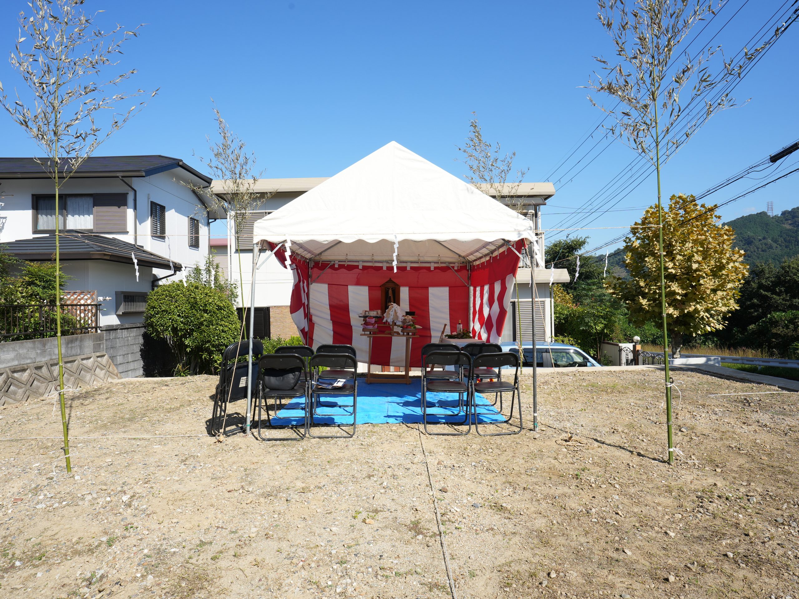 青空の下、住宅の建築予定地に設営された地鎮祭の風景。紅白幕を張ったテント内に祭壇が組まれ、周囲に忌竹としめ縄が張り巡らされています。