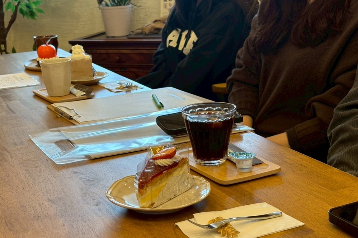 無垢材のテーブルにケーキやアイスコーヒーが用意され、リラックスしたカフェのような雰囲気の中で家づくりの打ち合わせをしている様子です。