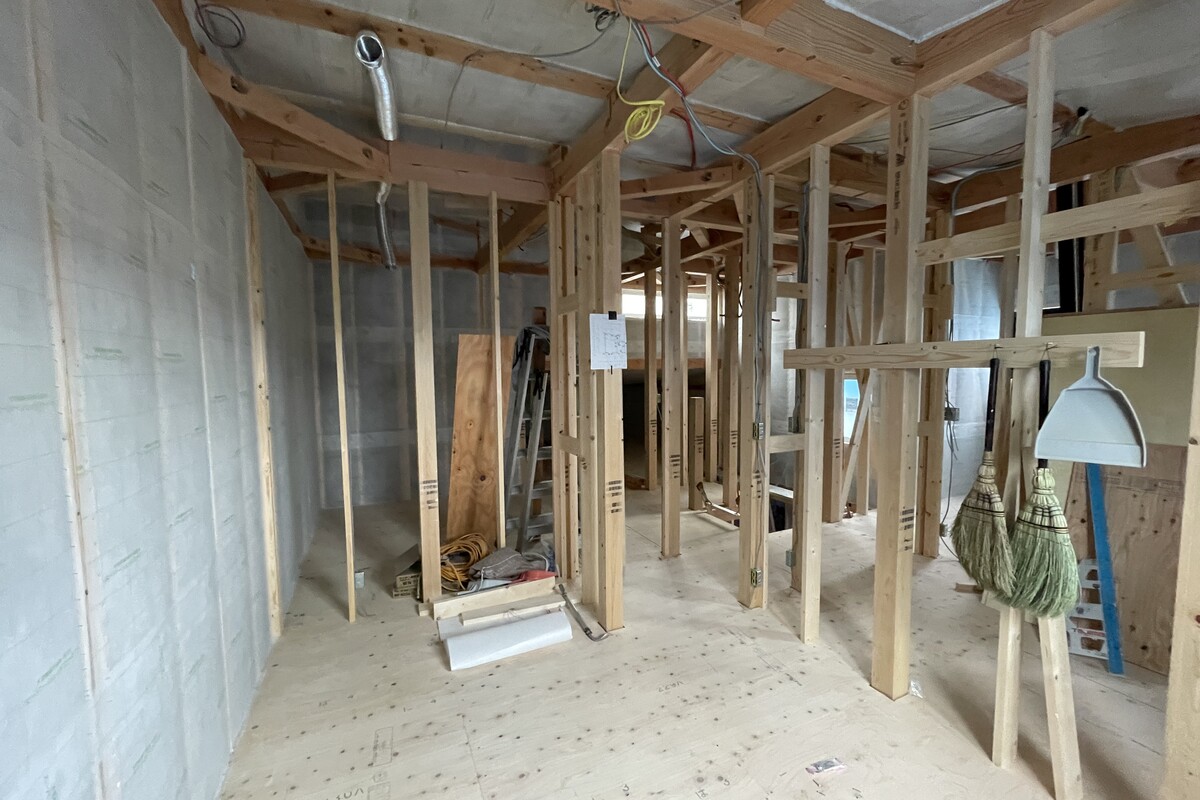 壁面に断熱材が施工され、柱や梁などの木造軸組が組み上げられた建築現場の様子。清掃用具が掛けられた整理整頓された現場から、丁寧な施工体制が伺えます。