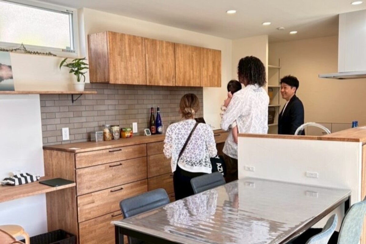 住宅完成見学会の現場で、木製キッチンカウンターや背面収納を丁寧に見学する家族と案内する工務店スタッフ