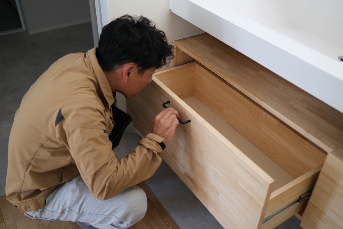 木の温もりが感じられる造作洗面化粧台で、職人またはスタッフが引き出しを開け、スムーズな動きや内部の仕上がりを丁寧に確認している様子です。