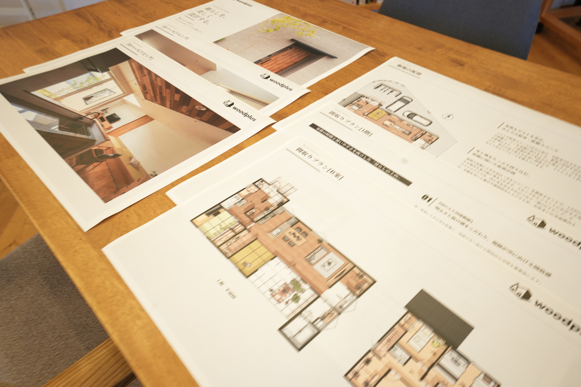 木目の美しいテーブルの上に広げられた住宅の平面図と3Dパース資料。吹き抜けリビングの完成イメージや敷地配置が確認できます。
