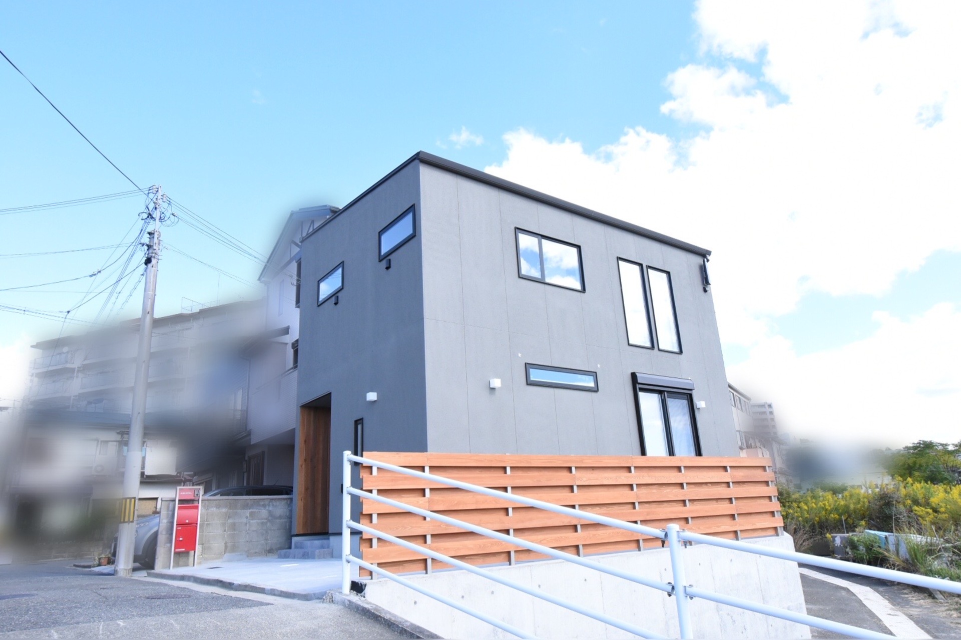グレーのシンプルな外壁に、木製ルーバーフェンスと木目調の玄関ドアがアクセントになったモダンな住宅の外観。
