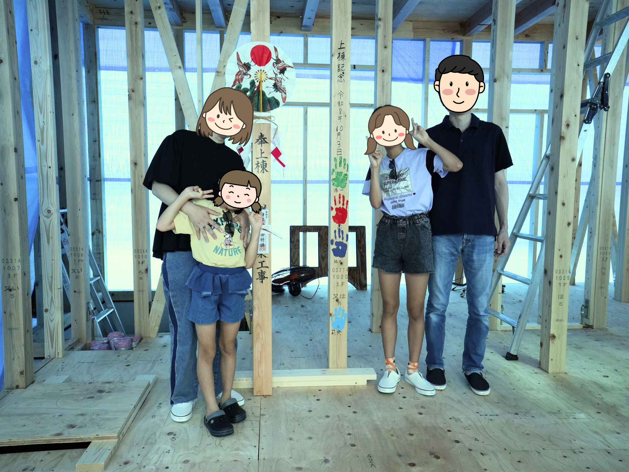 上棟と手形式を終えた建築現場で、お祝いの御幣やカラフルな家族の手形が記された構造柱を囲み、笑顔で記念撮影をする4人家族。木組みの梁や柱が露出した、家づくりの節目を感じる温かい光景。