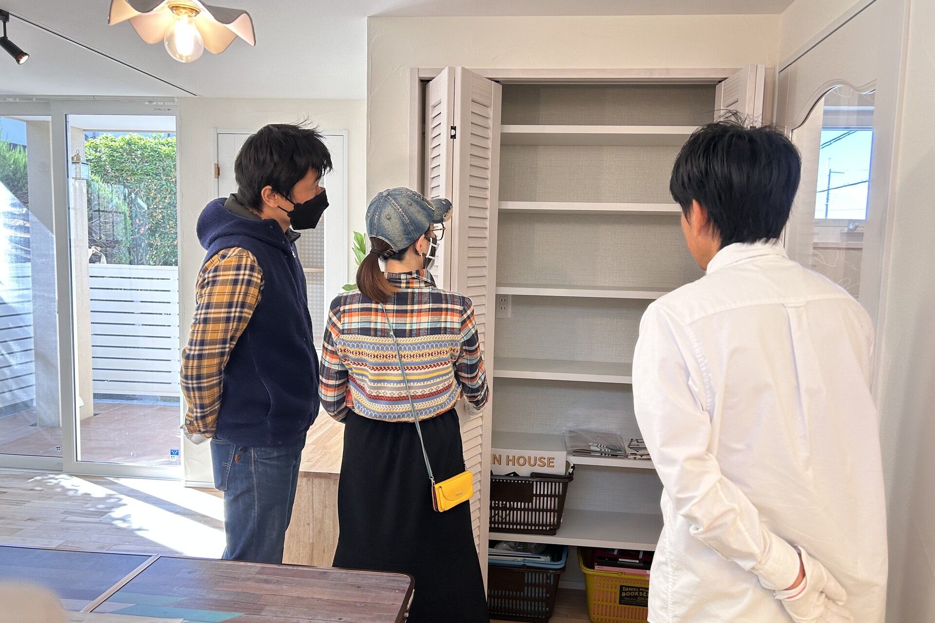 明るい室内で、ルーバー扉が特徴的な可動棚付きの収納スペースを見学しているお客様と案内スタッフ。