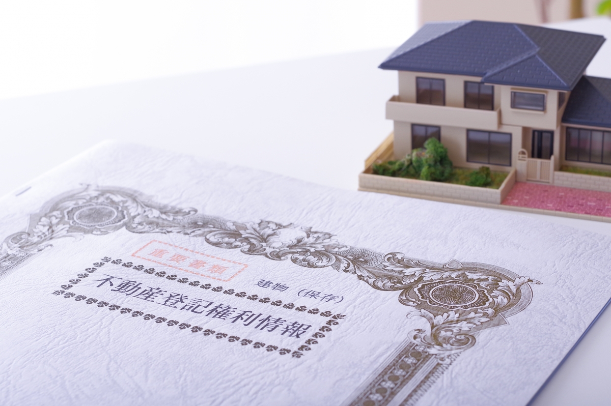 机の上に置かれた「不動産登記権利情報」の重要書類と戸建て住宅のミニチュア模型。