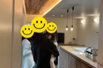 無垢材の板張り天井や間接照明が温かみのある空間を演出するLDKで、子どもを抱っこしながら新居を見学するご家族の後ろ姿。