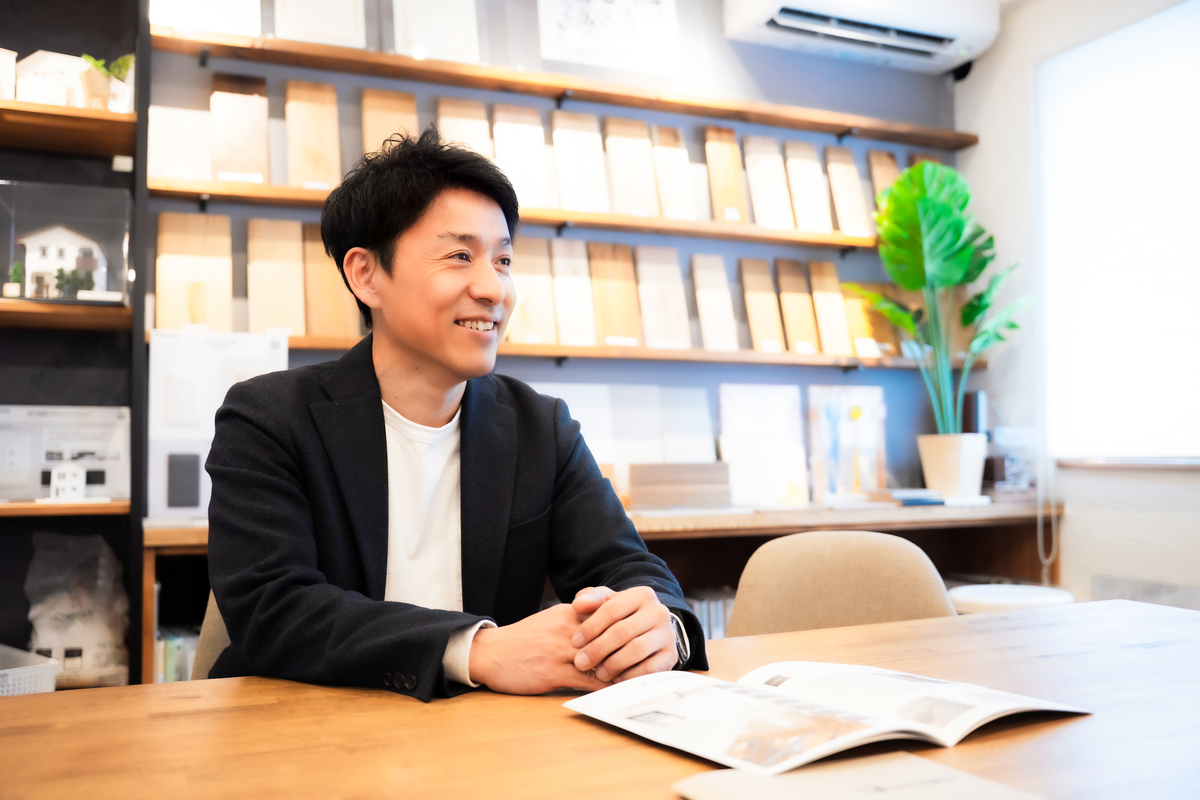 無垢材サンプルが並ぶ打ち合わせルームで、資料を前に穏やかな表情を浮かべる工務店スタッフ