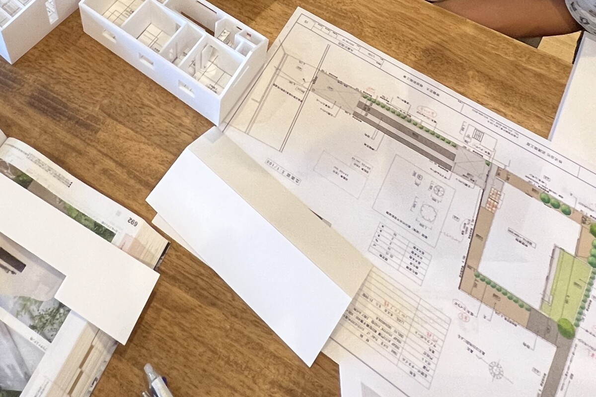 木製テーブルに広げられた外構や住宅の平面図と、間取りや空間のつながりを立体的に確認するための白い建築模型を用いた打ち合わせ風景。